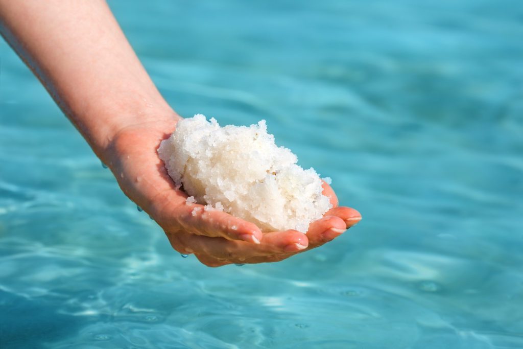 A woman holding a handful of salt from the Dead Sea with the sea in the background